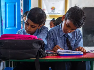 Two students writing at desks in an Indian school classroom